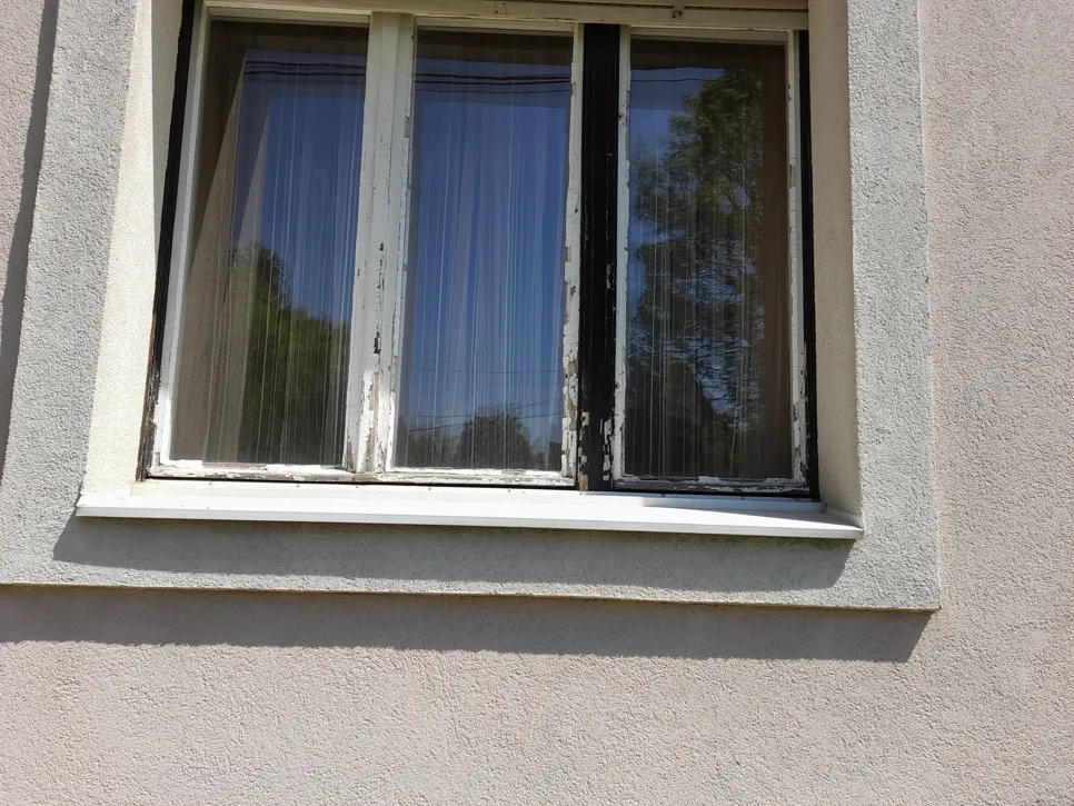 Lerakódó festék a külső ablakkereten Régi fa ablakkeret lerakódó festékkel a külső falon, ami időjárási károsodásra utal.