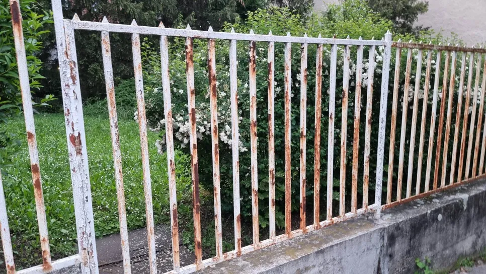Rozsdás fémkerítés a szabadban Régi fémkerítés, amelyet rozsda borít, egy buja zöld kert mellett. Figyelemre méltó korróziós és időjárási jelek.