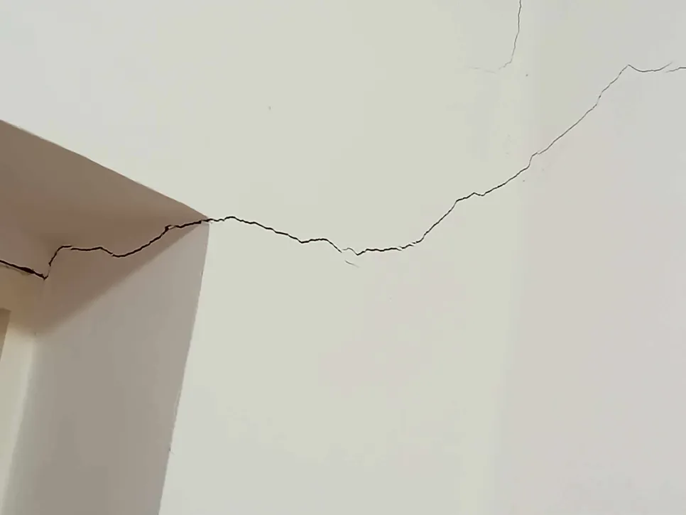 Cracks in an interior wall near a doorway suggest potential structural damage issues in the building.