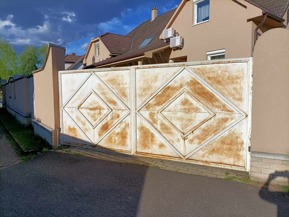 Rozsdás fémkapu Nagy fémkapu, amelyen súlyos rozsda látható, befolyásolva a funkcionalitást és a megjelenést egy lakóövezetben.