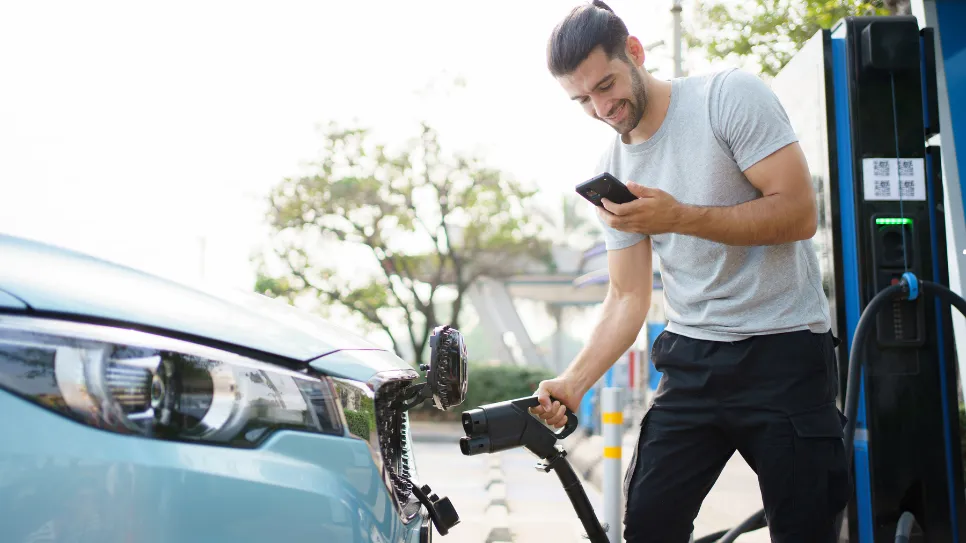 Elektromos-autó töltése töltőállomáson Egy férfi elektromos autóját tölti egy nyilvános töltőállomáson, miközben a telefonját használja.