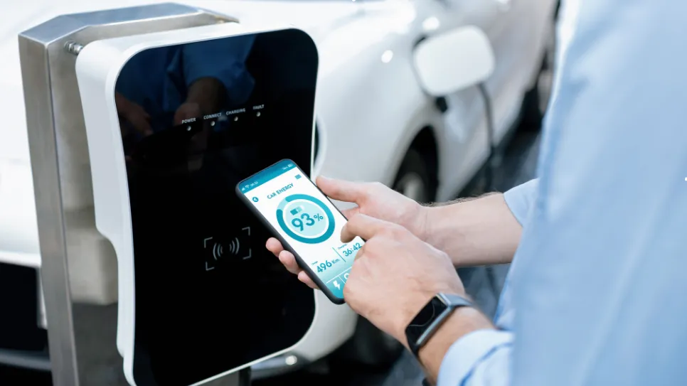Elektromos autó töltésének ellenőrzése mobilon Egy férfi telefonján ellenőrzi elektromos autója töltöttségi szintjét, miközben a jármű egy töltőállomáson csatlakozik.