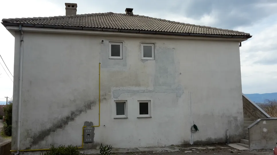 A penész növekedése látható egy ház külső falán, két kis ablak alatt, ami nedvességi problémákra utal.